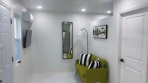 A hallway with a green sofa, a mirror, a floor lamp, and a framed abstract artwork. - Seda Verde (Kissimmee)