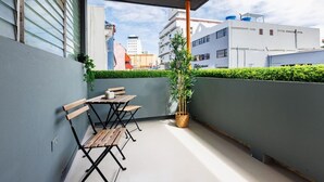 Ein Balkon mit Holztisch und -stühlen, einem Blumentopf und Blick auf umliegende Gebäude.
