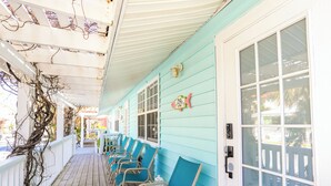 A covered porch with wooden flooring and teal chairs.