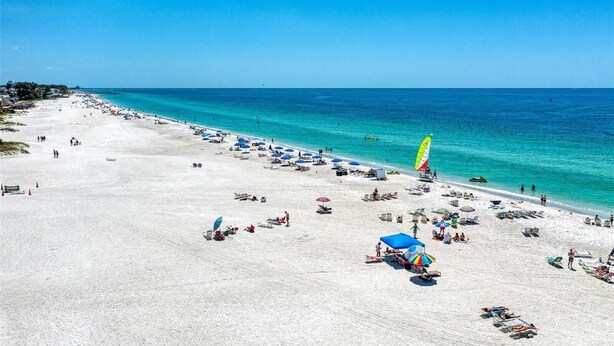 A wide beach with numerous sun loungers and umbrellas, a clear blue sky, and a calm sea.