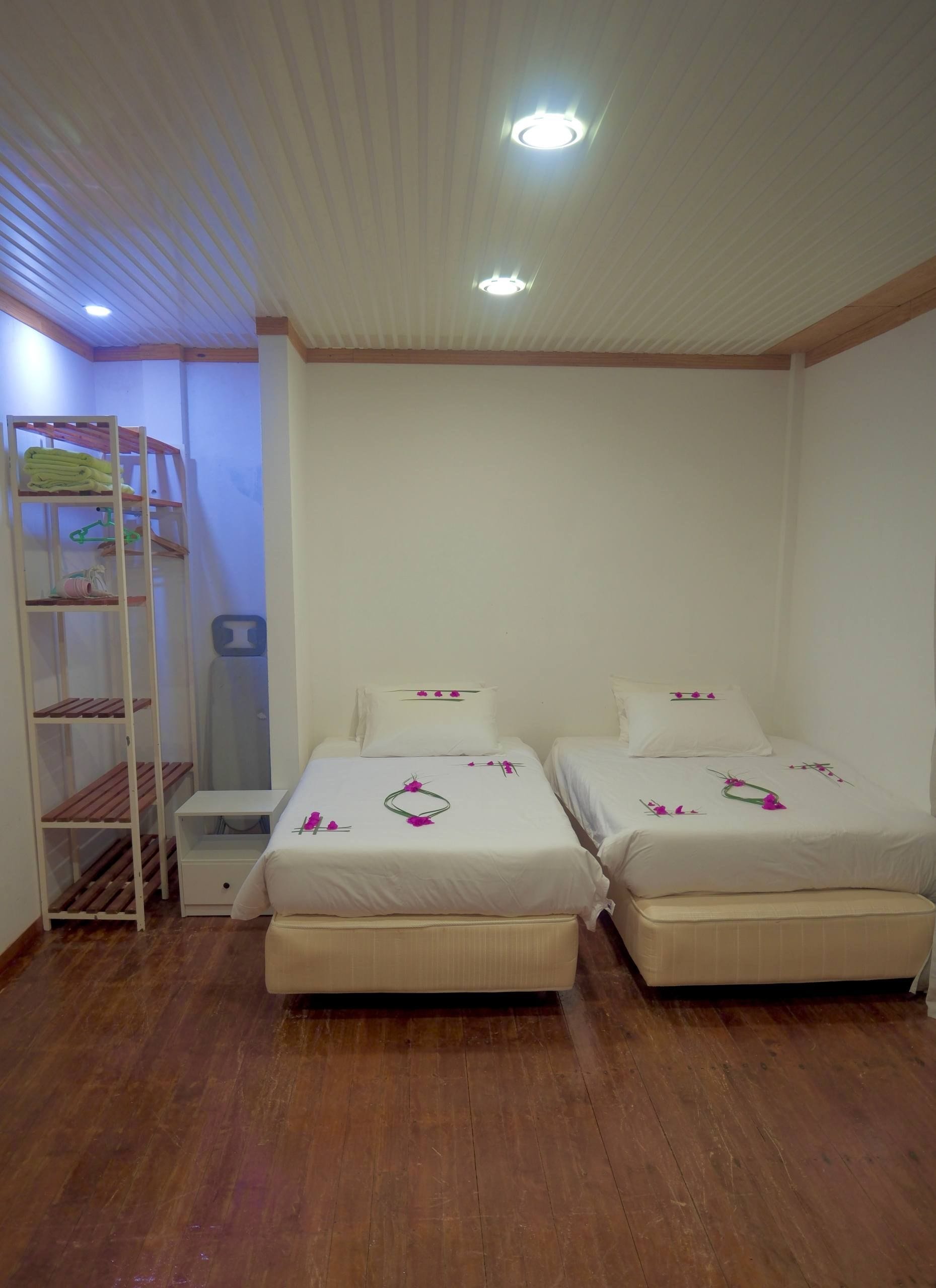 A room with two beds, a wooden floor, and a white ceiling with a light fixture.