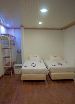 A room with two beds, a wooden floor, and a white ceiling with a light fixture. - AHI Maldives (Omadhoo)