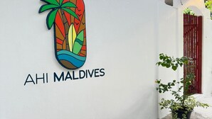 A white wall with a colorful palm tree logo and the text "AHI MALDIVES". - AHI Maldives (Omadhoo)
