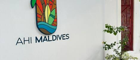 Un muro bianco con un logo colorato a forma di palma e la scritta 'AHI MALDIVES'.