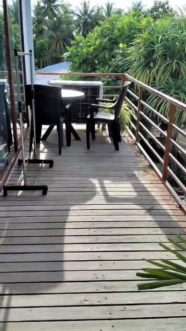 Een houten terras met een tafel en stoelen, omringd door metalen hekken en weelderige begroeiing.