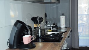 A modern kitchen with a coffee maker, a pink mug, a frying pan, and various utensils on the counter. - Balcony in the center, Netflix & free coffee/tea (Chemnitz)