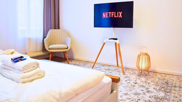 A hotel room with a bed, a chair, a TV on a stand, a lamp, and a radiator. - Balcony in the center, Netflix & free coffee/tea (Chemnitz)