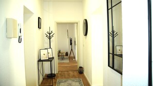 A hallway with a wooden floor, framed pictures on a stand, a rug, and a tripod in the background. - Balcony in the center, Netflix & free coffee/tea (Chemnitz)