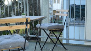 A patio area with a table and two chairs, a small potted plant, and a view of a building through a metal gate. - Balcony in the center, Netflix & free coffee/tea (Chemnitz)