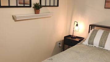 A bedroom with a bed, a nightstand, a wall-mounted shelf with a plant, and two arched windows.