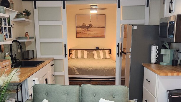 A compact living space with a sofa, a dining table, a kitchen area, and a bed with a sliding door. - BRAND NEW! 1-bedroom apartment in the beautiful historic village of Greene, NY (Greene)