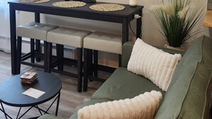 A modern living room with a dark wooden dining table, a green sofa with fluffy cushions, and a small round coffee table. - BRAND NEW! 1-bedroom apartment in the beautiful historic village of Greene, NY (Greene)