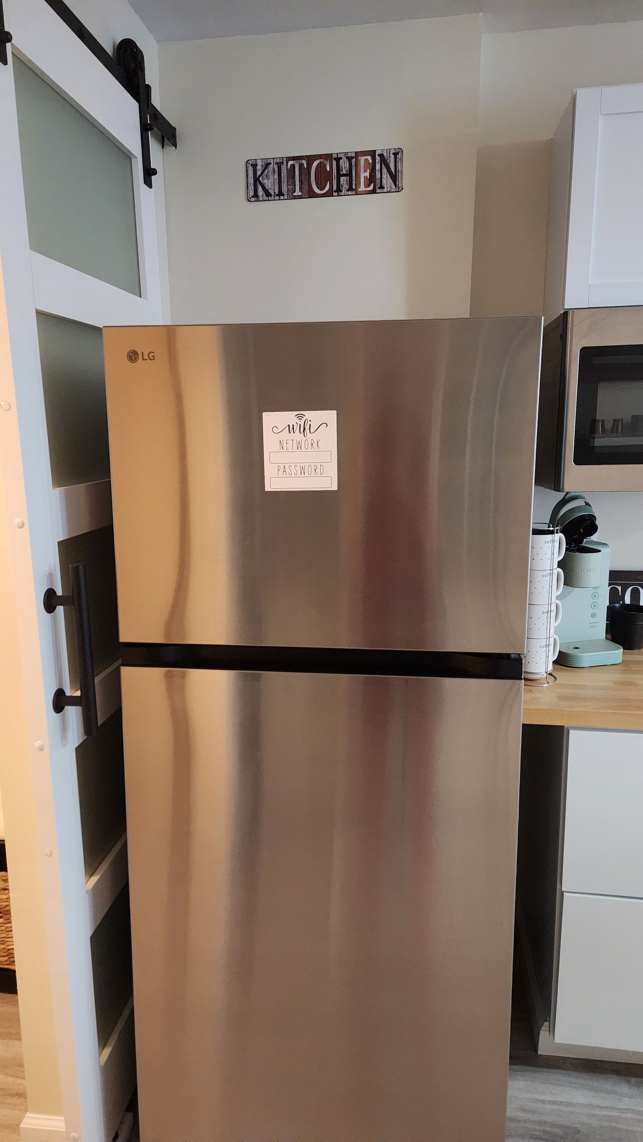 Un refrigerador de acero inoxidable con un cartel del código de la red WiFi, un letrero de cocina arriba y una cafetera sobre la encimera.