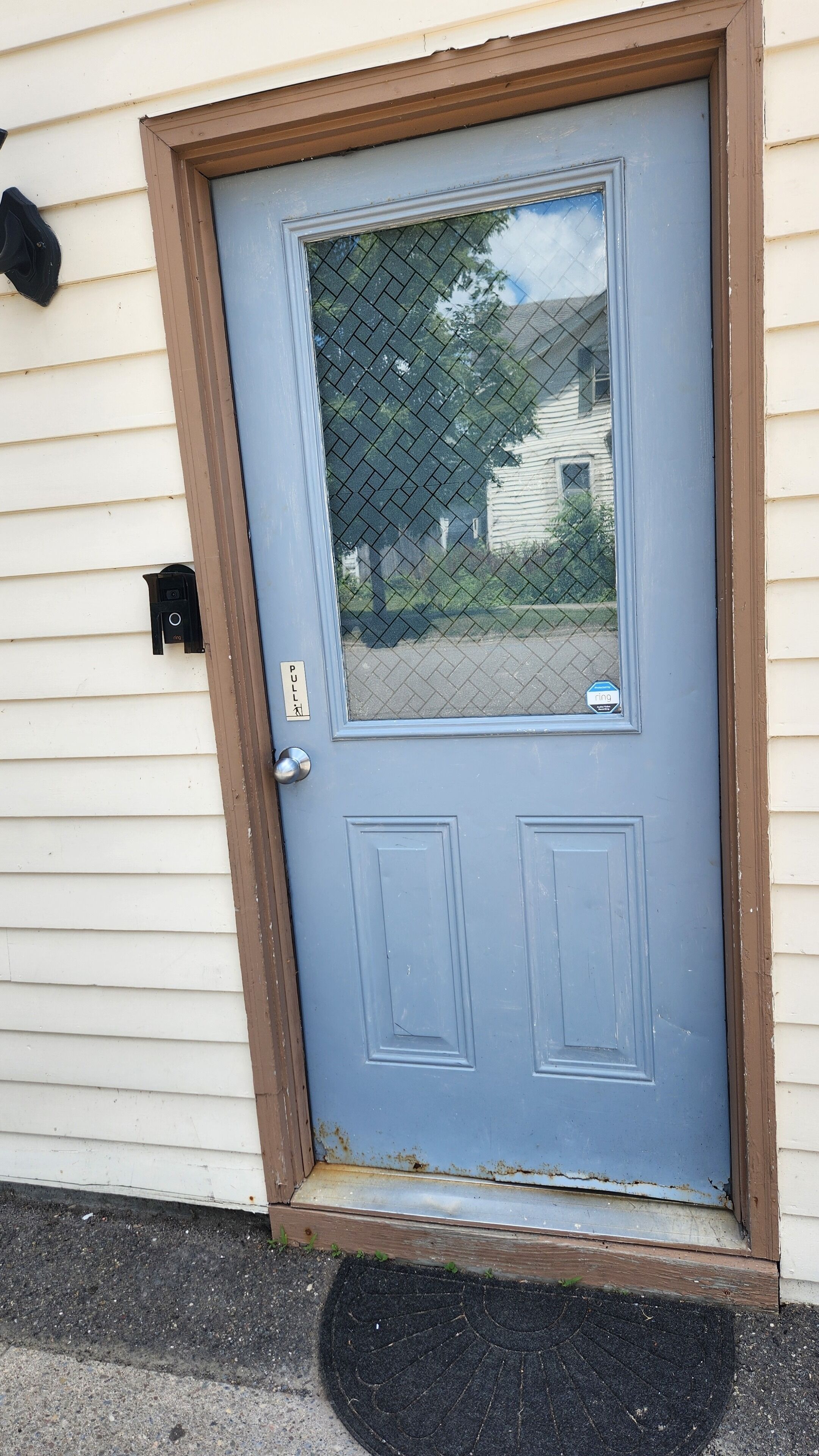 A blue door with a small window, a mailbox, and a doormat.