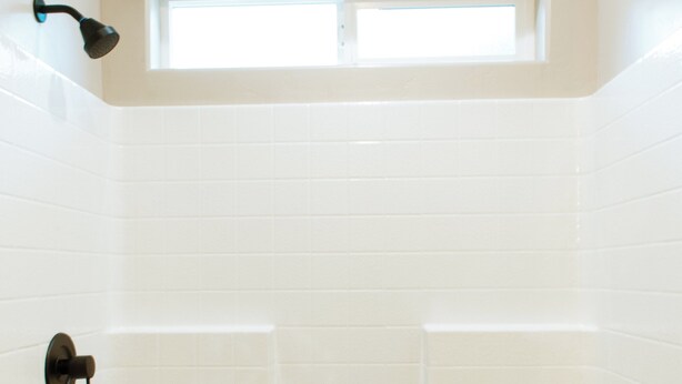 Ein Badezimmer mit weiß gefliesten Wänden, einem Fenster und einer Dusche mit Abfluss.