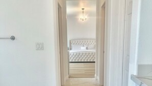 A hallway with a marble floor leading to a bedroom with a tufted headboard and a chandelier.