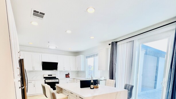 A modern kitchen with white cabinets, a central island with bar stools, and a large window with curtains.