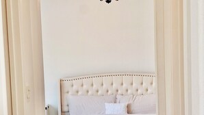 A bedroom with a tufted headboard, a bed with white linens, and a wooden floor.