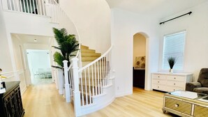 A spacious living area with a curved staircase, a dining area, and a view of the kitchen.