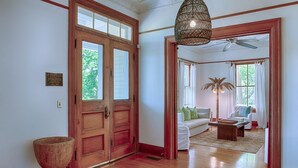 A spacious room with a wooden floor, a large wooden door, and a ceiling fan. - Officers Row - Elegant historic mansion w/pool steps from beach (Tybee Island)