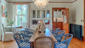 A dining area with a wooden table and blue wicker chairs, a chandelier, and white cabinets in the background. - Officers Row - Elegant historic mansion w/pool steps from beach (Tybee Island)