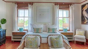 A bedroom with a bed, two bedside tables, a chair, and a large window with curtains. - Officers Row - Elegant historic mansion w/pool steps from beach (Tybee Island)