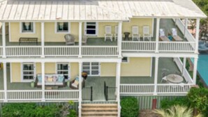 A two-story house with a balcony, surrounded by lush greenery and a view of the ocean. - Officers Row - Elegant historic mansion w/pool steps from beach (Tybee Island)