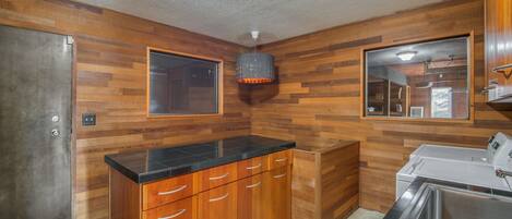A kitchen with wooden panel walls, a black countertop, stainless steel appliances, and a window.