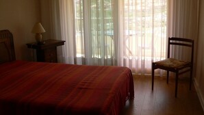 Un dormitorio con cama, una silla, una mesita de noche y una ventana con cortinas.