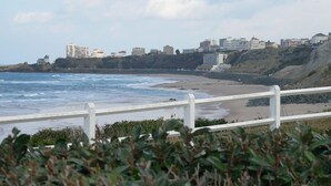 Vista costera con una valla blanca, playa y edificios al fondo.