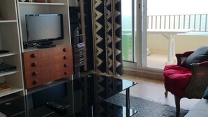 Habitación de hotel con balcón, televisión, mueble de madera y alfombra estampada.