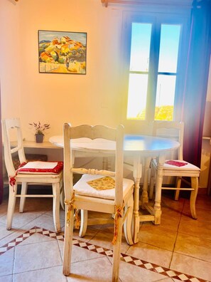 Un'area pranzo con un tavolo rotondo e quattro sedie, ognuna dotata di un cuscino bianco. Sopra il tavolo è appeso un quadro.