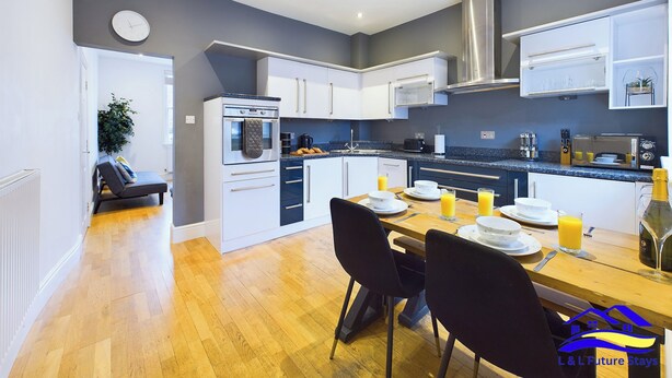 A modern kitchen with white cabinets, a built-in oven, and a dining area with a wooden table and chairs. - 2br-sleeps4-citycentre-freeparking (Derby)