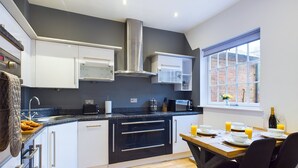 A modern kitchen with white and black cabinetry, a stainless steel range hood, and a breakfast setup with orange juice and a bottle of champagne. - 2br-sleeps4-citycentre-freeparking (Derby)
