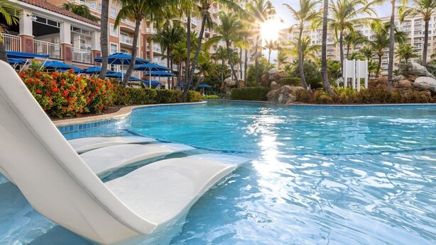 Une piscine avec un toboggan, entourée de palmiers et bordée d’un bâtiment doté de balcons.
