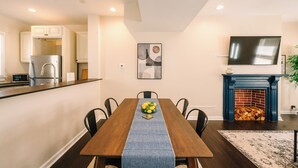 A dining room with a wooden table, chairs, a blue table runner, a fireplace, and a kitchen in the background. - Peaceful Pittsburgh Escape! Mins to North Shore, AGH, PNC Park, Rivers Casino! (Pittsburgh)