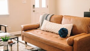 A brown leather sofa with a white and blue pillow, a glass coffee table with a plant, and a door in the background. - Peaceful Pittsburgh Escape! Mins to North Shore, AGH, PNC Park, Rivers Casino! (Pittsburgh)