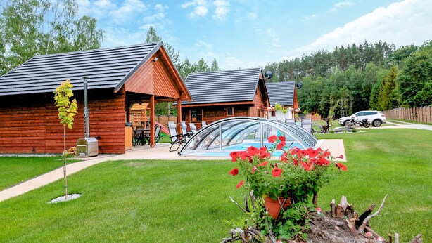 Une cabane en bois dotée d’un patio fermé par des baies vitrées, d’une piscine et d’une voiture garée à proximité.