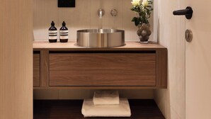 Uma casa de banho moderna com toucador de madeira, lavatório de aço inoxidável e espelho acima.