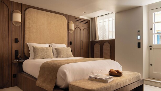 Quarto com cama grande, painéis de madeira, mesa de cabeceira com um livro e janela com cortinas.