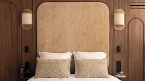 Quarto de hotel com uma cama grande, duas luminárias na parede e cabeceira de madeira.