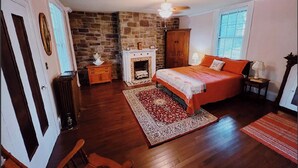 Un dormitorio con chimenea de piedra, una cama con ropa de cama naranja, un armario de madera y una mesita de noche con lámpara.