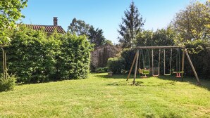 A grassy backyard with a swing set and a stone building in the background.
