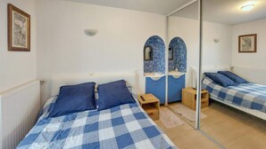 A bedroom with two beds, a mirror, a small bedside table, and a blue-tiled sink.