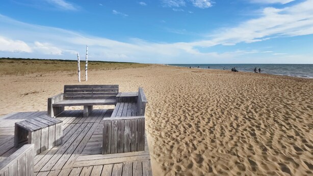 A wooden deck leading to a beach with a clear view of the ocean and a sandy shore.