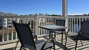 A covered outdoor patio with a table and chairs, overlooking a body of water and buildings in the background. - Myrtlewood Condo-Covered Porch, Pool & Hot Tub (Myrtle Beach)