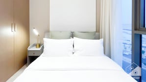 Ein Hotelzimmer mit Bett, Nachttisch, Lampe und Blick auf die Stadt durch ein Fenster.