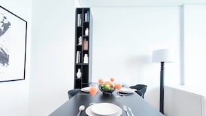 A modern dining area with a black table, white plates, and a fruit bowl. - Cozy 1BR With Balcony & Views in Azizi Fawad (Dubai)