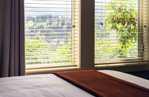 Une chambre d’hôtel avec un lit, une fenêtre avec des stores et une vue sur la verdure environnante.