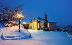 Una casa cubierta de nieve con una entrada iluminada y un camino de entrada también nevado.